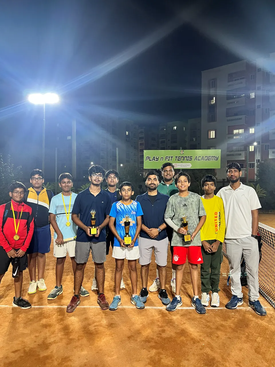 PLAY n FIT players and coaches with trophies on court at night under a floodlight